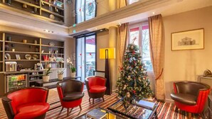 Un vestíbulo de hotel con un árbol de Navidad, sillas rojas, una máquina de café y una estantería.