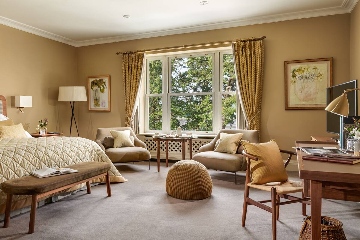 Un dormitorio elegante con una cama grande, un escritorio, una silla, una mesita y una ventana con cortinas.