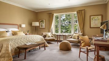 A well-appointed bedroom with a large bed, a desk, a chair, a small table, and a window with curtains.