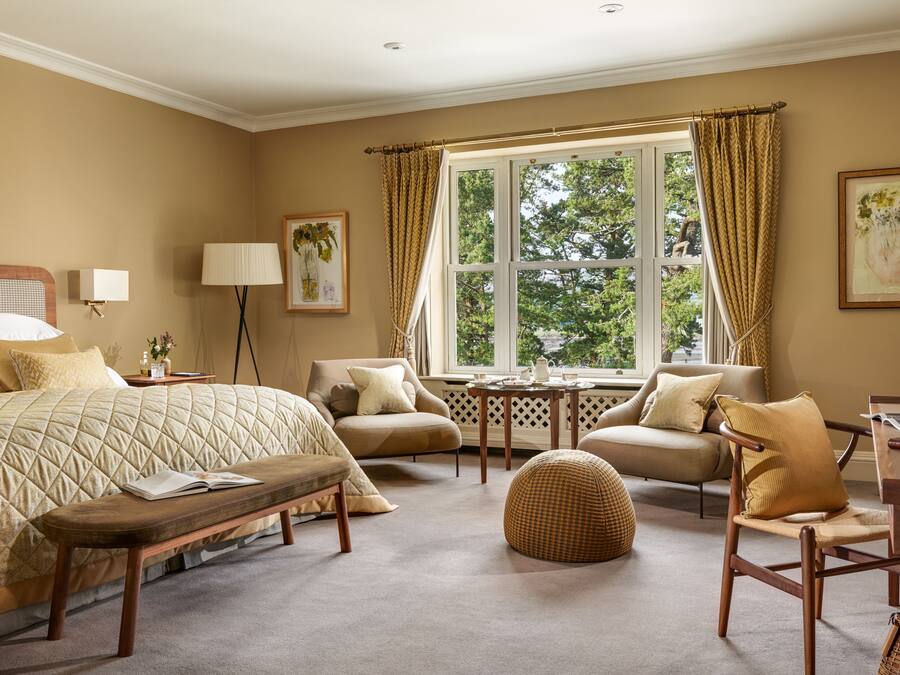 A well-appointed bedroom with a large bed, a desk, a chair, a small table, and a window with curtains.