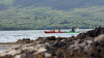 Three kayaks on a calm body of water with a rocky shoreline and a green hillside in the background.
