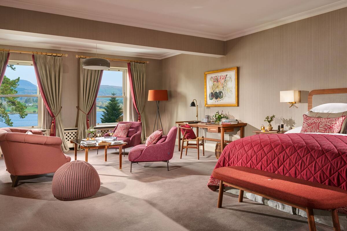 Habitación de hotel con una cama grande, un escritorio, dos sillas, un banco y vistas a un lago.
