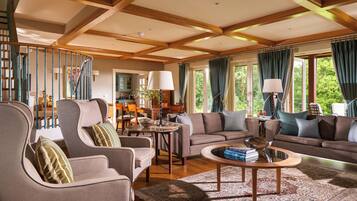 A spacious living room with a high ceiling, wooden beams, a dining area, and large windows with curtains.
