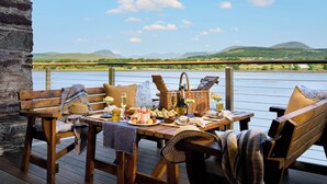 A wooden deck with a table set for a meal, overlooking a river and hills. - Sheen Falls Lodge (Kenmare)