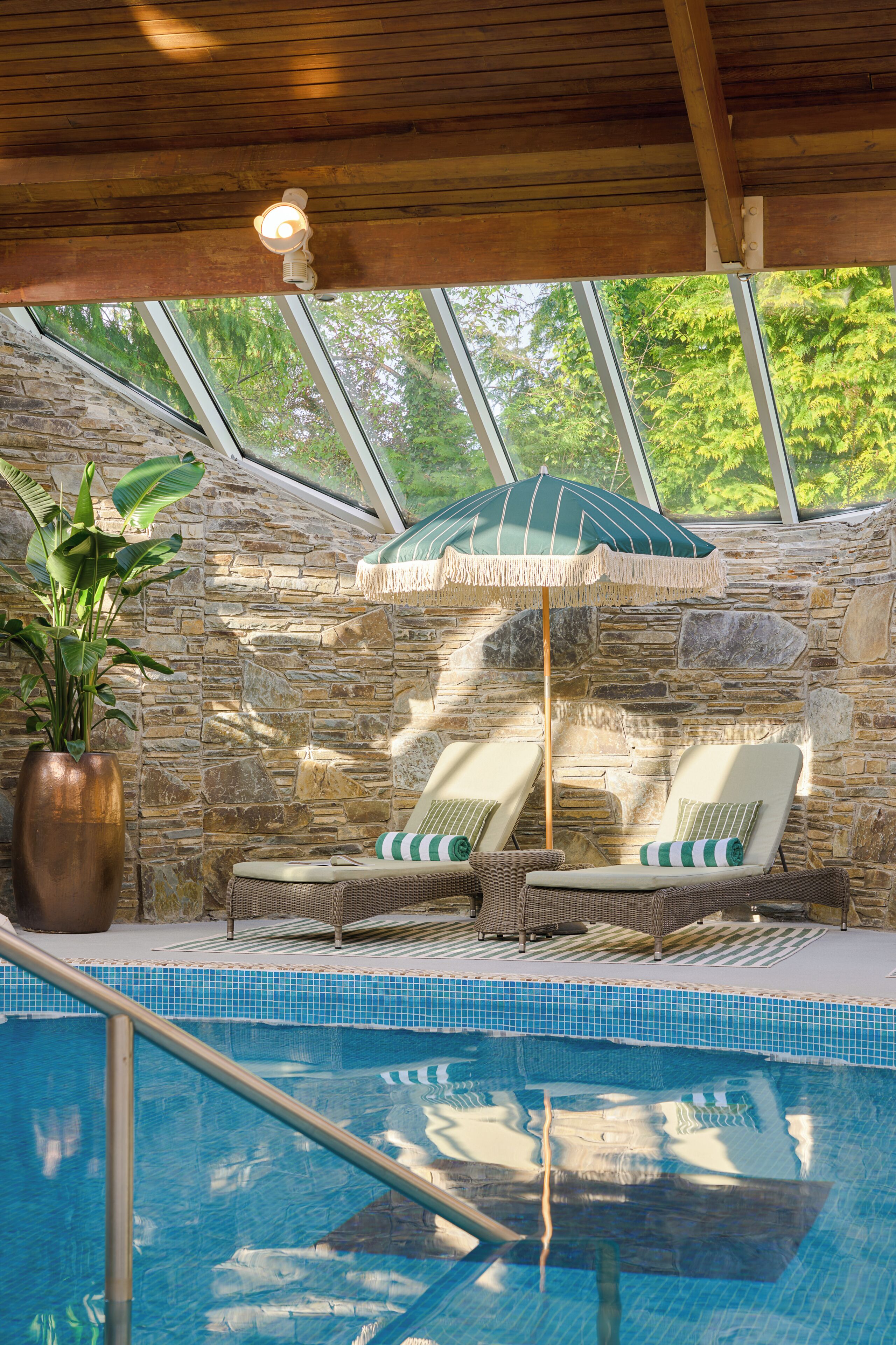 A pool area with lounge chairs, a stone wall, and a large potted plant.