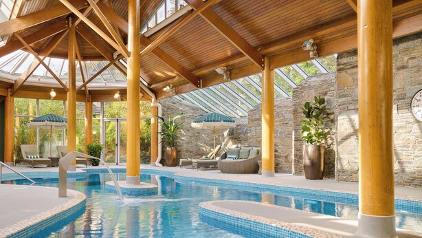 Una piscina interior con vigas de madera, paredes de piedra y zonas de estar con sombrillas.