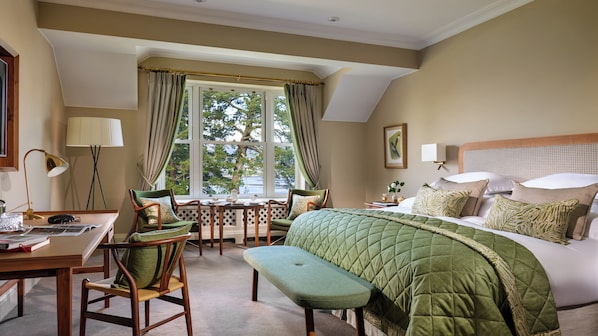 A hotel room with a bed, a desk, chairs, a window with curtains, and a view of trees.