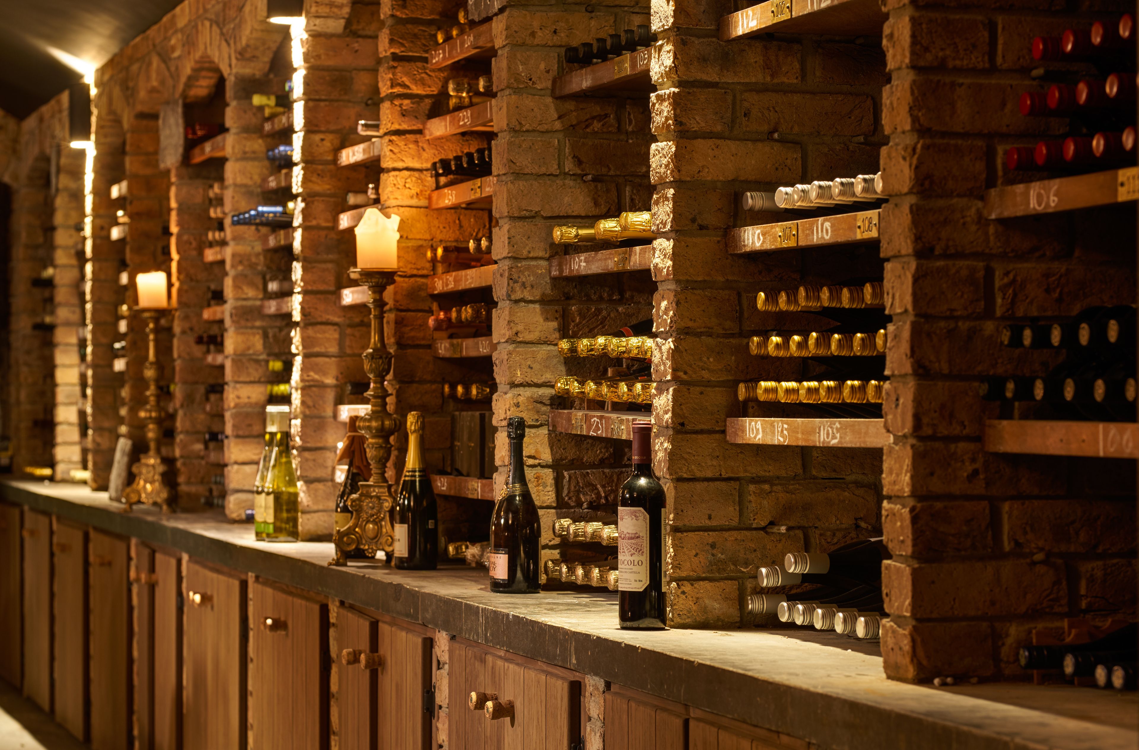 A wine cellar with wooden shelves and bottles, including a prominent bottle labeled "Chardonnay 2010".