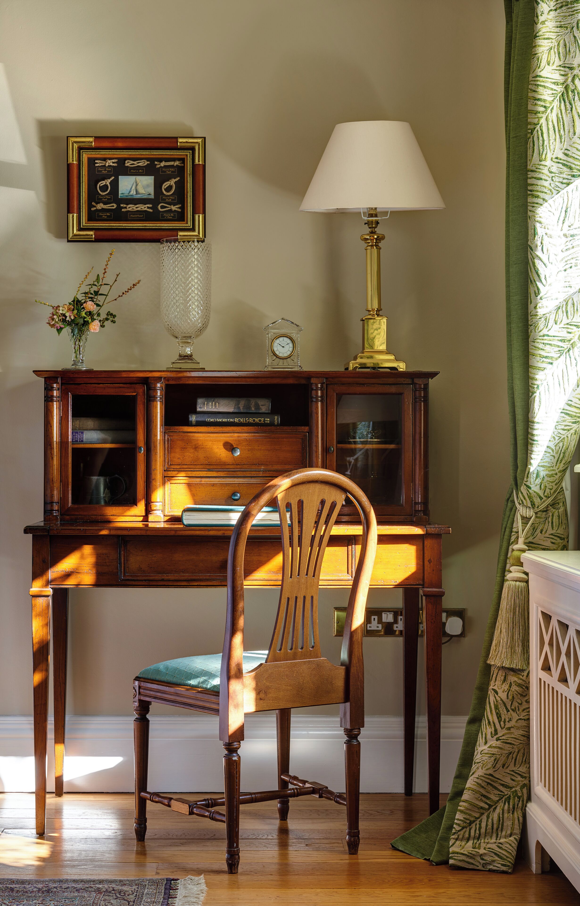 A wooden desk with a lamp, a chair, and a framed picture on the wall.