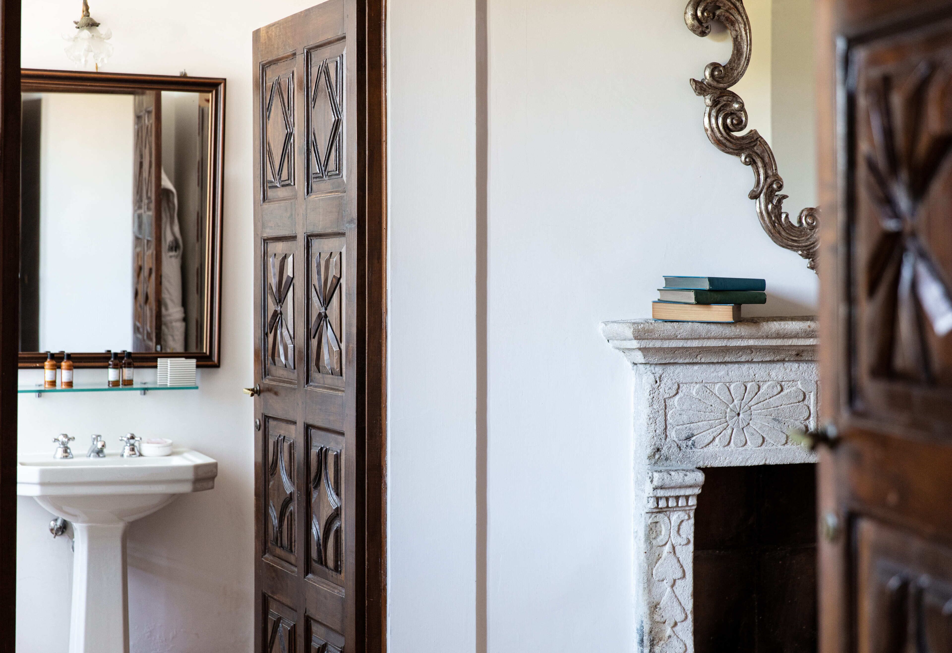 A bathroom with a white sink, a mirror, and a wooden door with intricate carvings.