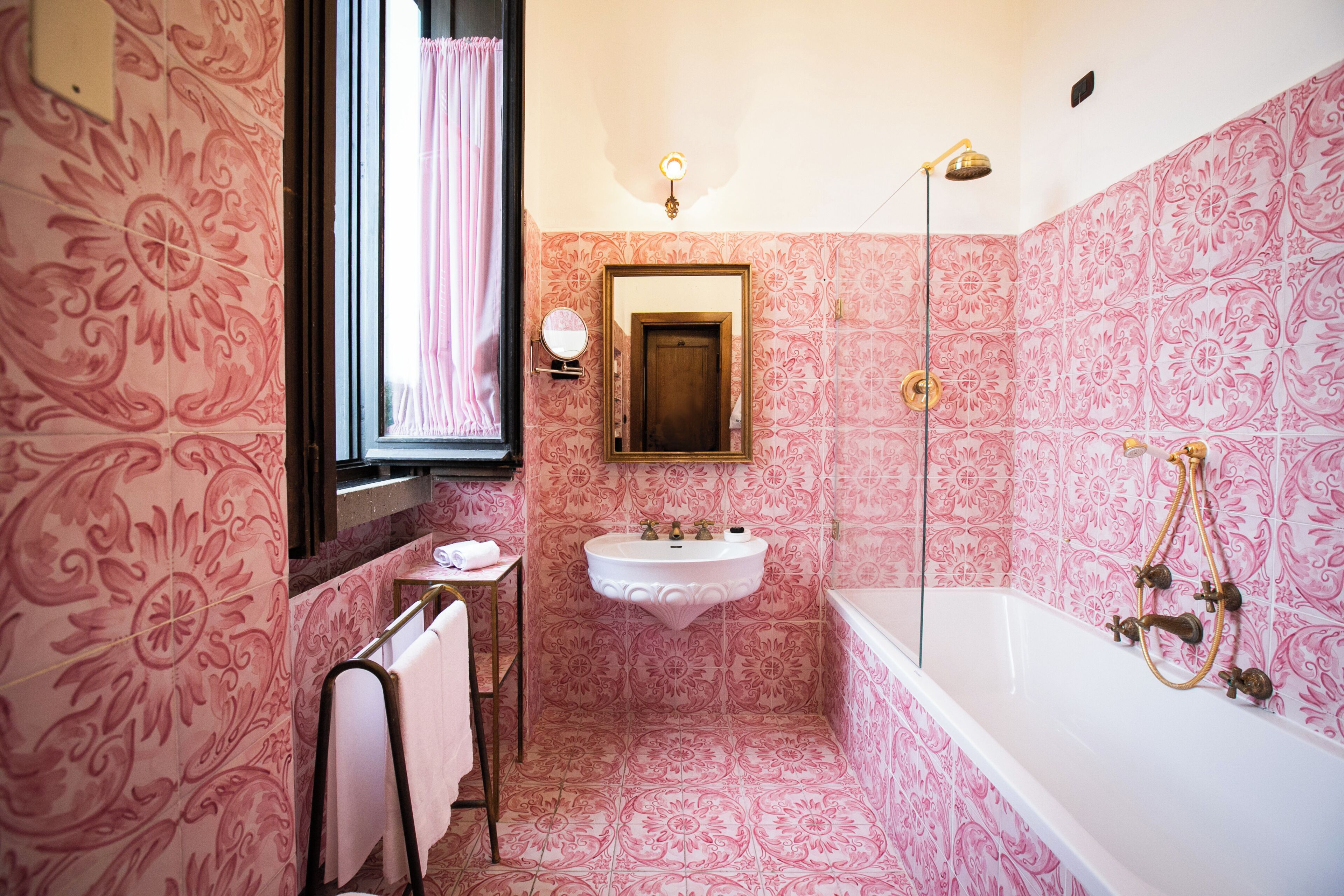 Un baño con papel tapiz estampado, un lavamanos, un espejo, un perchero para toallas y una bañera.