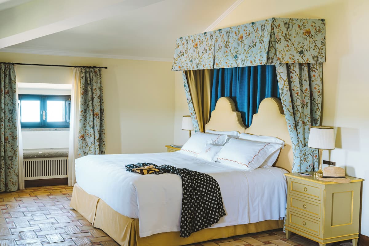 A bedroom with a bed, curtains, a nightstand, and a radiator.