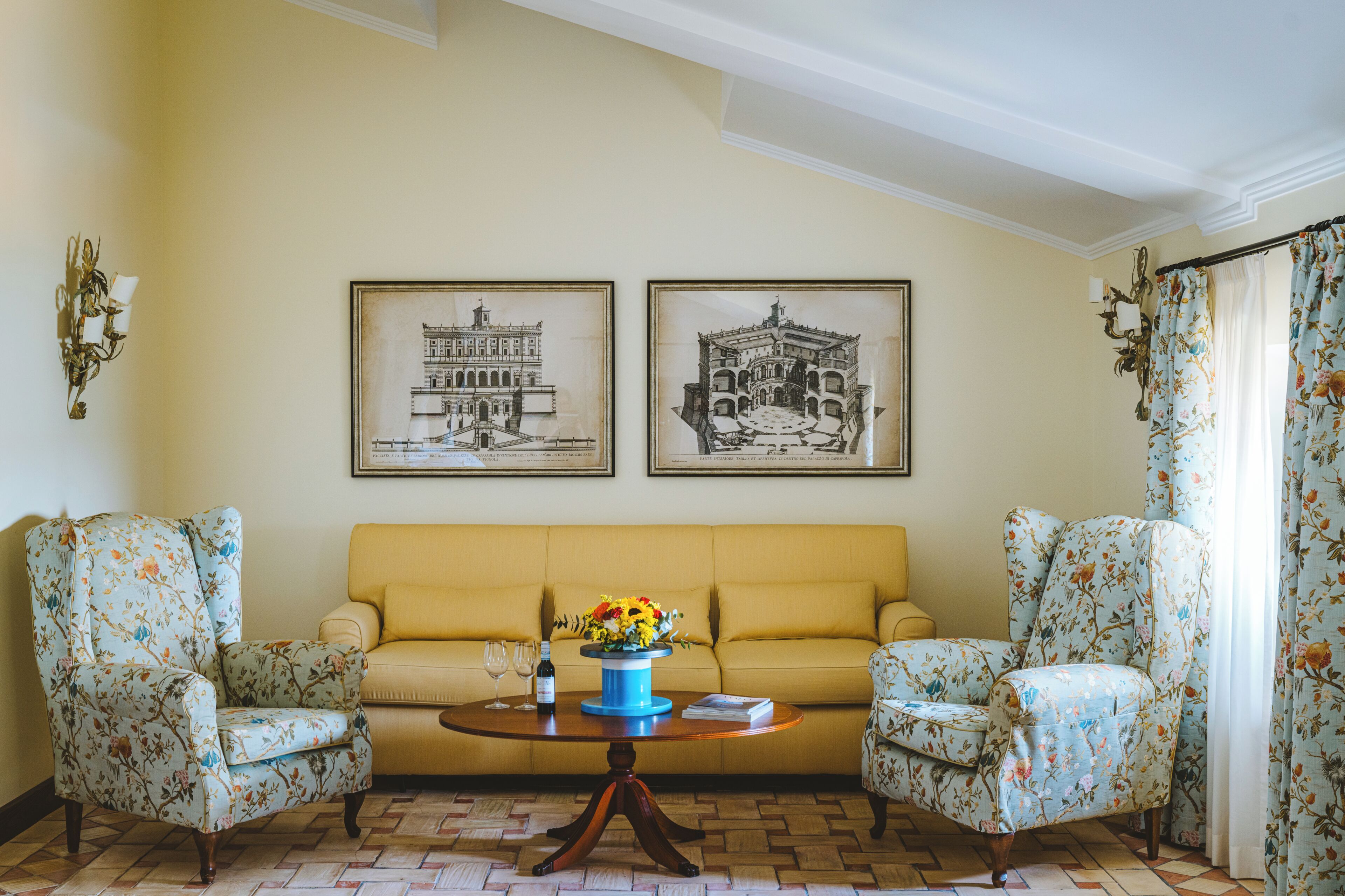 Une pièce comprenant un canapé, deux fauteuils, une table basse avec un vase, et deux tableaux encadrés accrochés au mur.