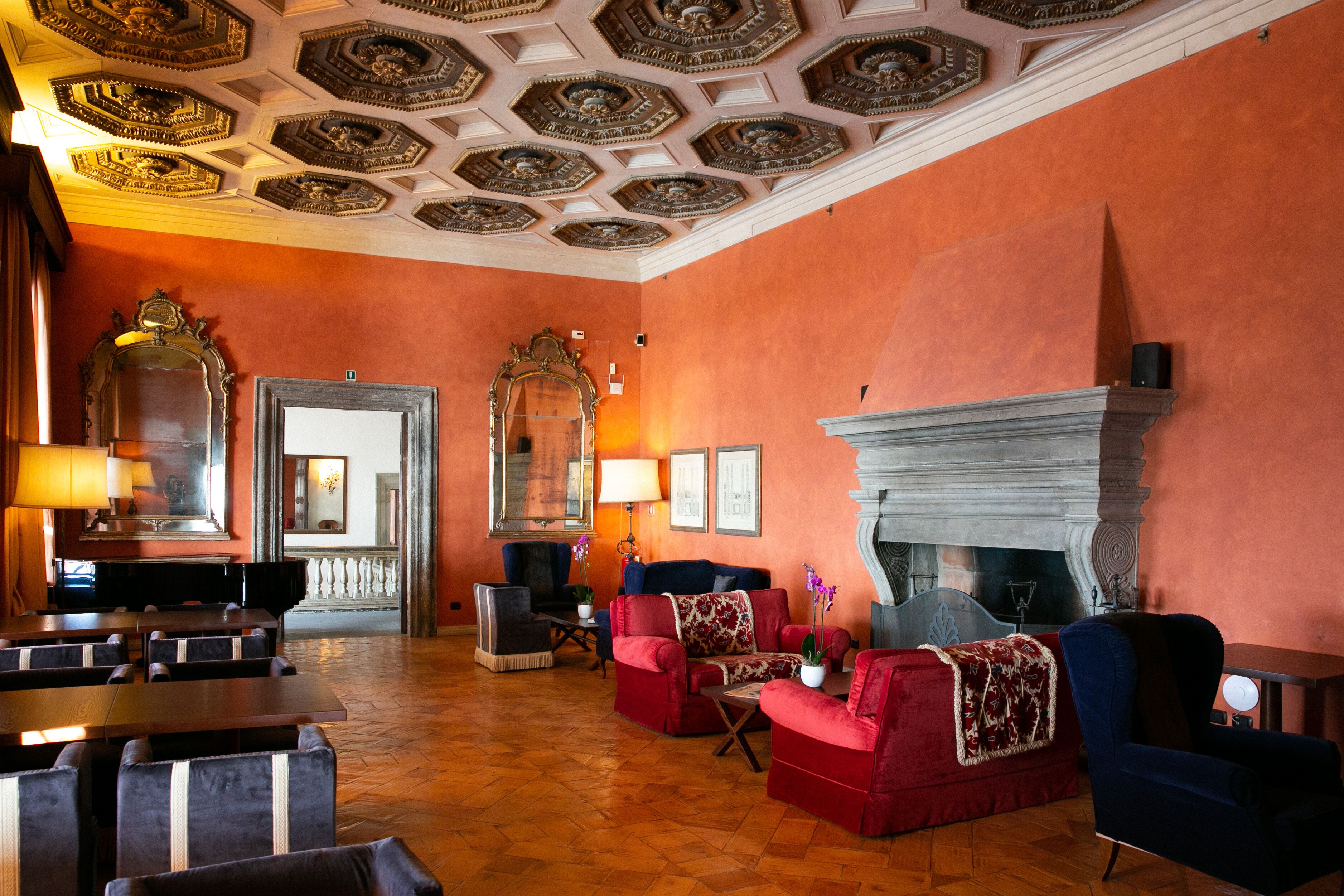 A hotel lobby with a fireplace, red sofas, and a dining area with tables and chairs.