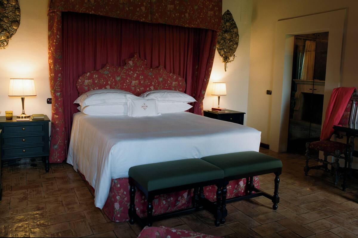A bedroom with a large bed, two bedside tables with lamps, a bench, and a chair.