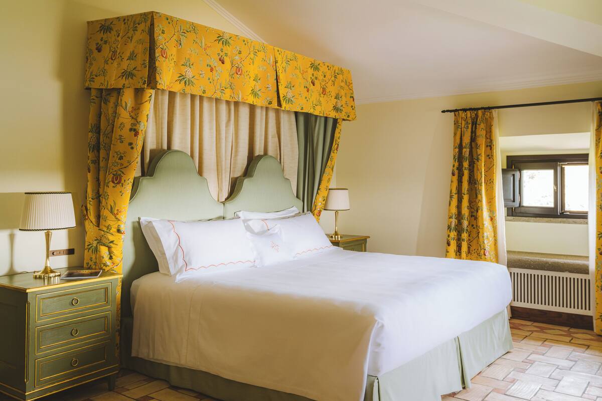 A bedroom with a four-poster bed, two bedside tables, and a window with curtains.