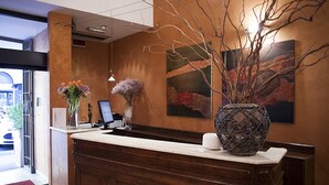 A reception desk with a vase of flowers, a coffee cup, and a painting on the wall. - Hotel Columbia (Rome)