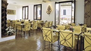 A dining area with yellow chairs and tables, large windows, and a wooden ceiling. - Hotel Columbia (Rome)