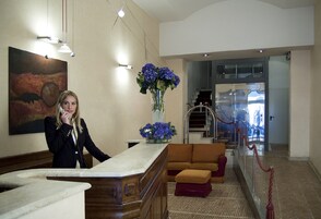 A reception area with a marble counter, a vase of flowers, a sofa, and a staircase in the background.