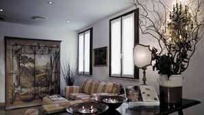 A living room with a sofa, a table with candles, a large painting, and a vase with branches. - Hotel Columbia (Rome)