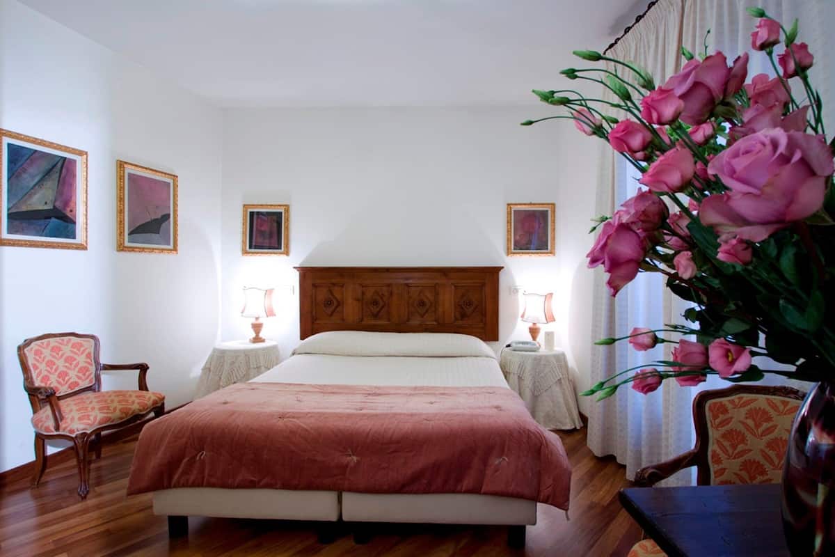 A bedroom with a wooden bed, two bedside tables with lamps, a chair, and a vase of flowers.