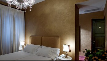A hotel room with a large bed, two bedside tables, a chandelier, and a door with a small window.