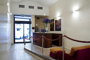 Eine Hotellobby mit einer Rezeption, einem Blumenstrauß, einem Gemälde an der Wand und einer roten Absperrschlange.