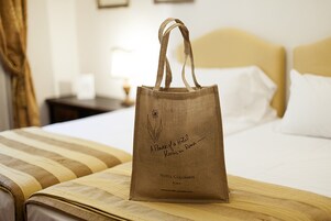 En brun tote-taske med tekst ligger på en seng i et hotelværelse.