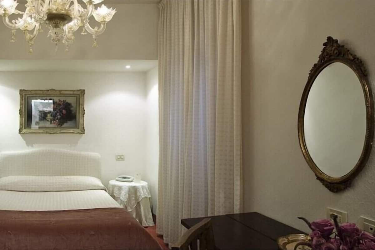 A bedroom with a large bed, a chandelier, a mirror, and a framed picture on the wall.