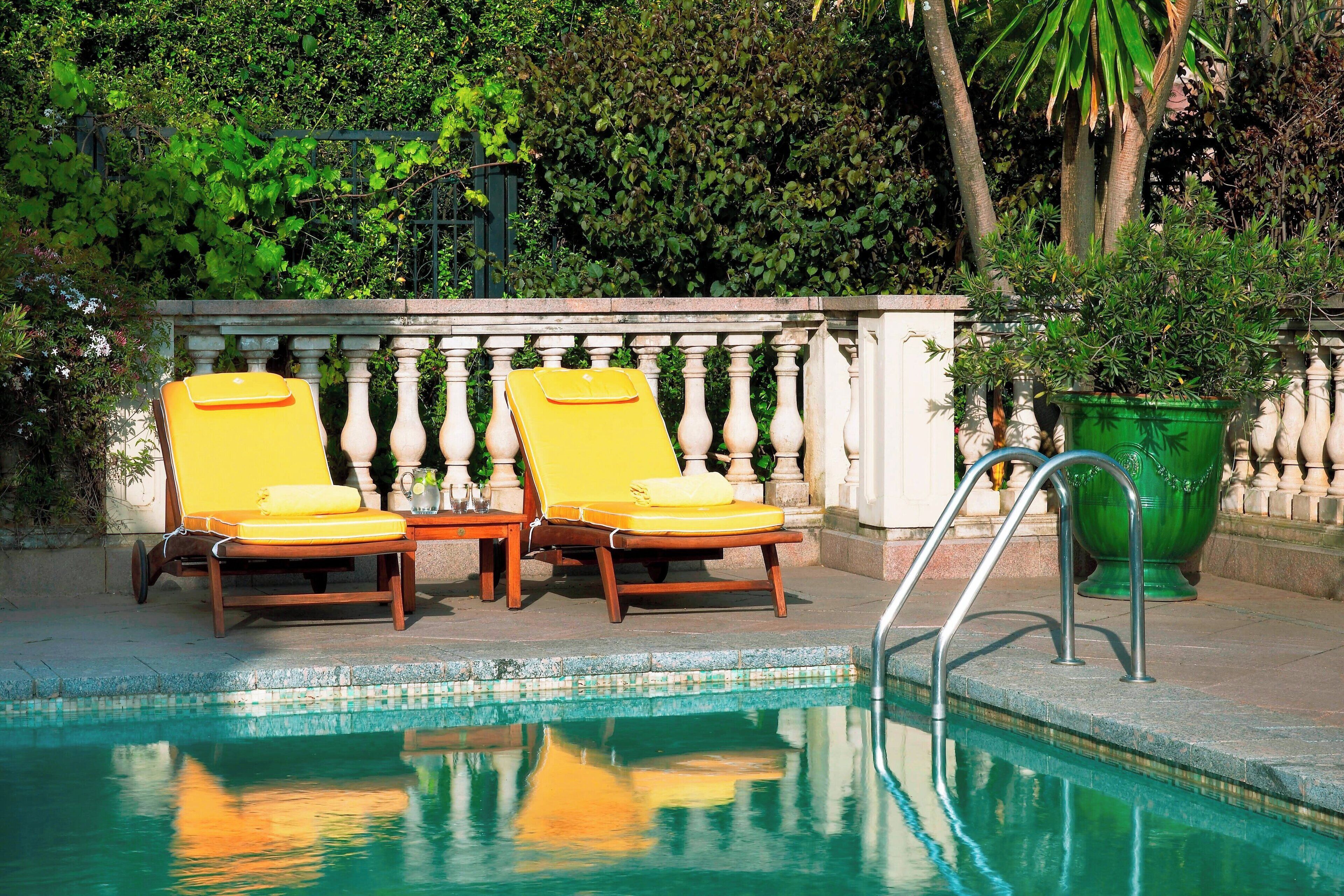 Un espace aménagé au bord de la piscine, avec deux chaises longues en bois et une plante verte en pot.