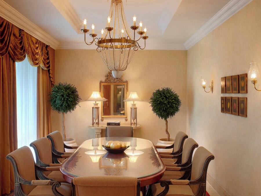 A formal dining room with a large oval table, six chairs, a chandelier, wall-mounted lamps, and framed pictures.