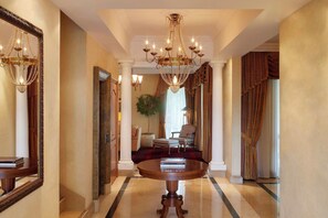 A grand hallway with a large chandelier, a round table with books, and a potted plant.