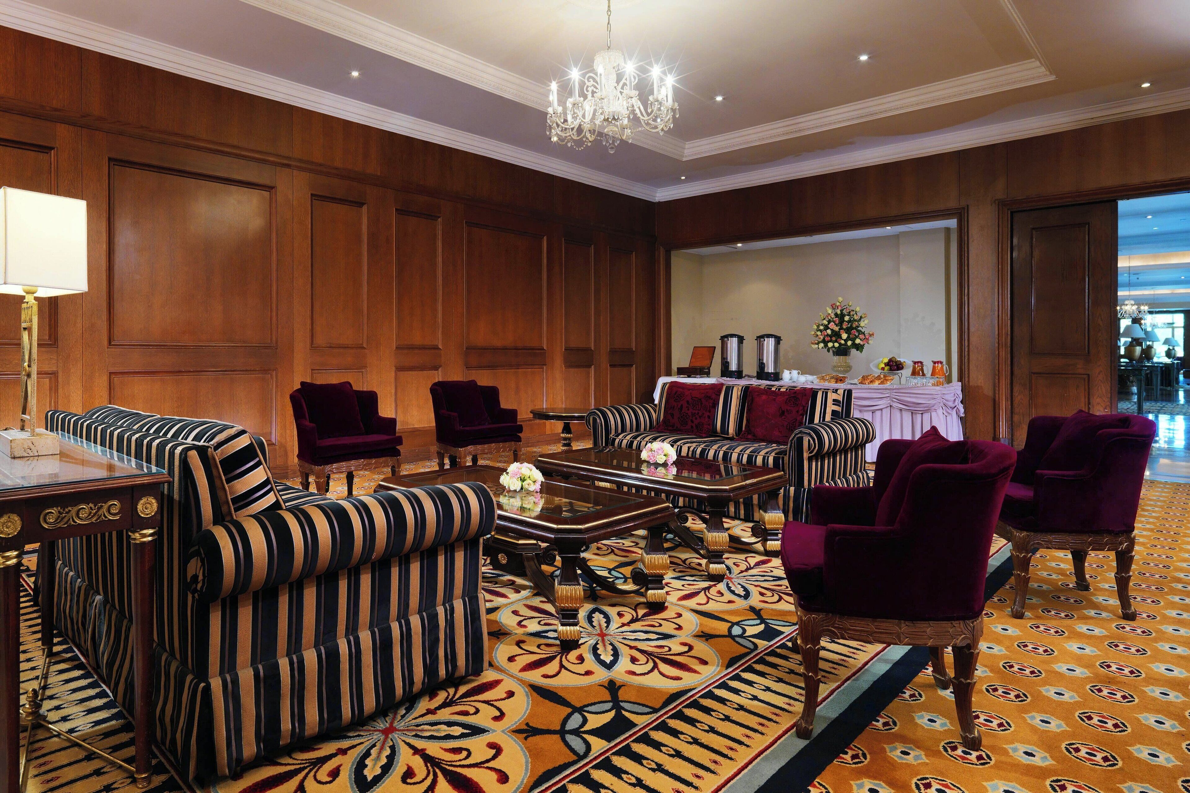 Eine geräumige Lobby mit einem großen Kronleuchter, gestreiften Sofas und einem gemusterten Teppich.