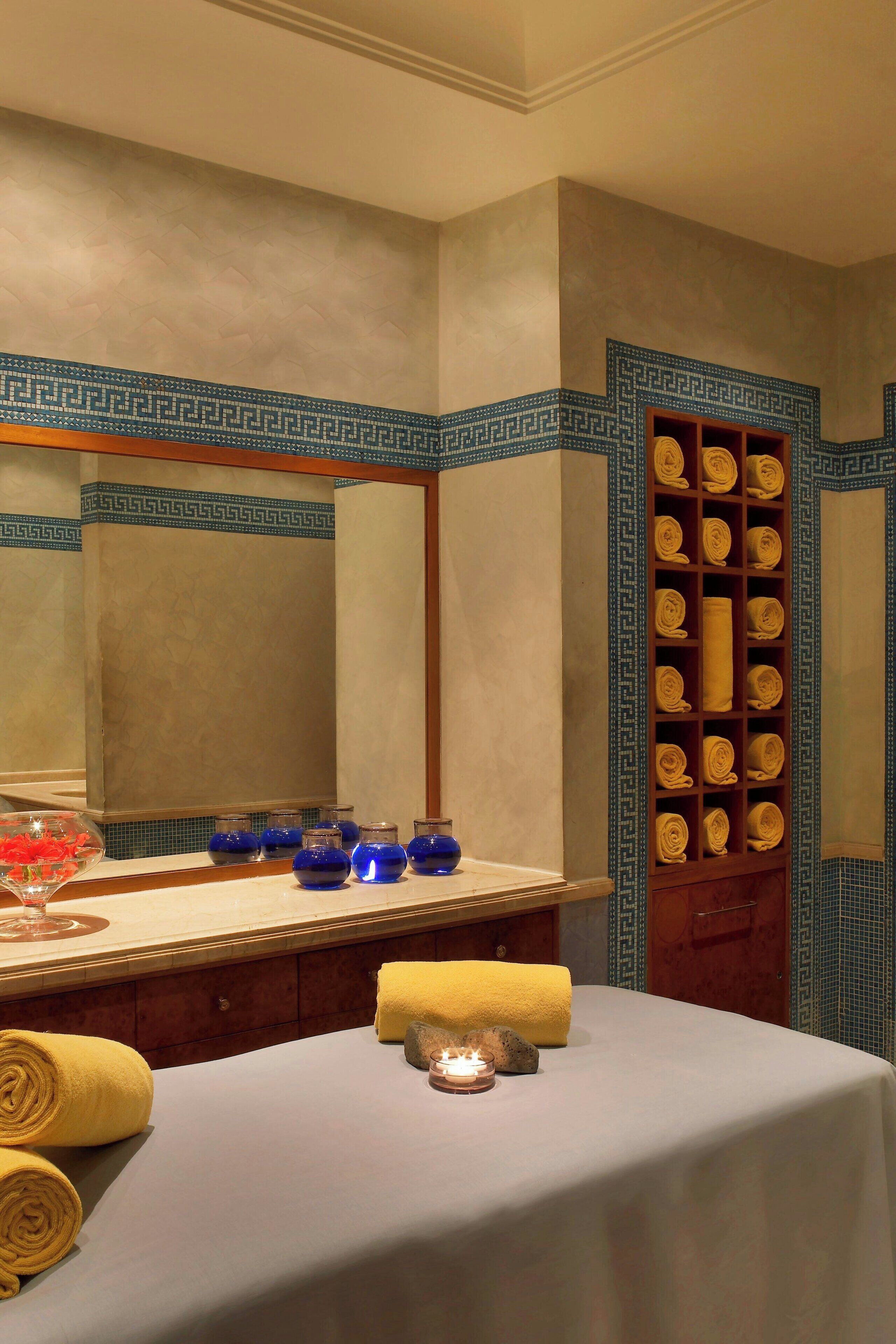 A spa room with a massage table, towels, candles, and a shelf with neatly rolled towels.