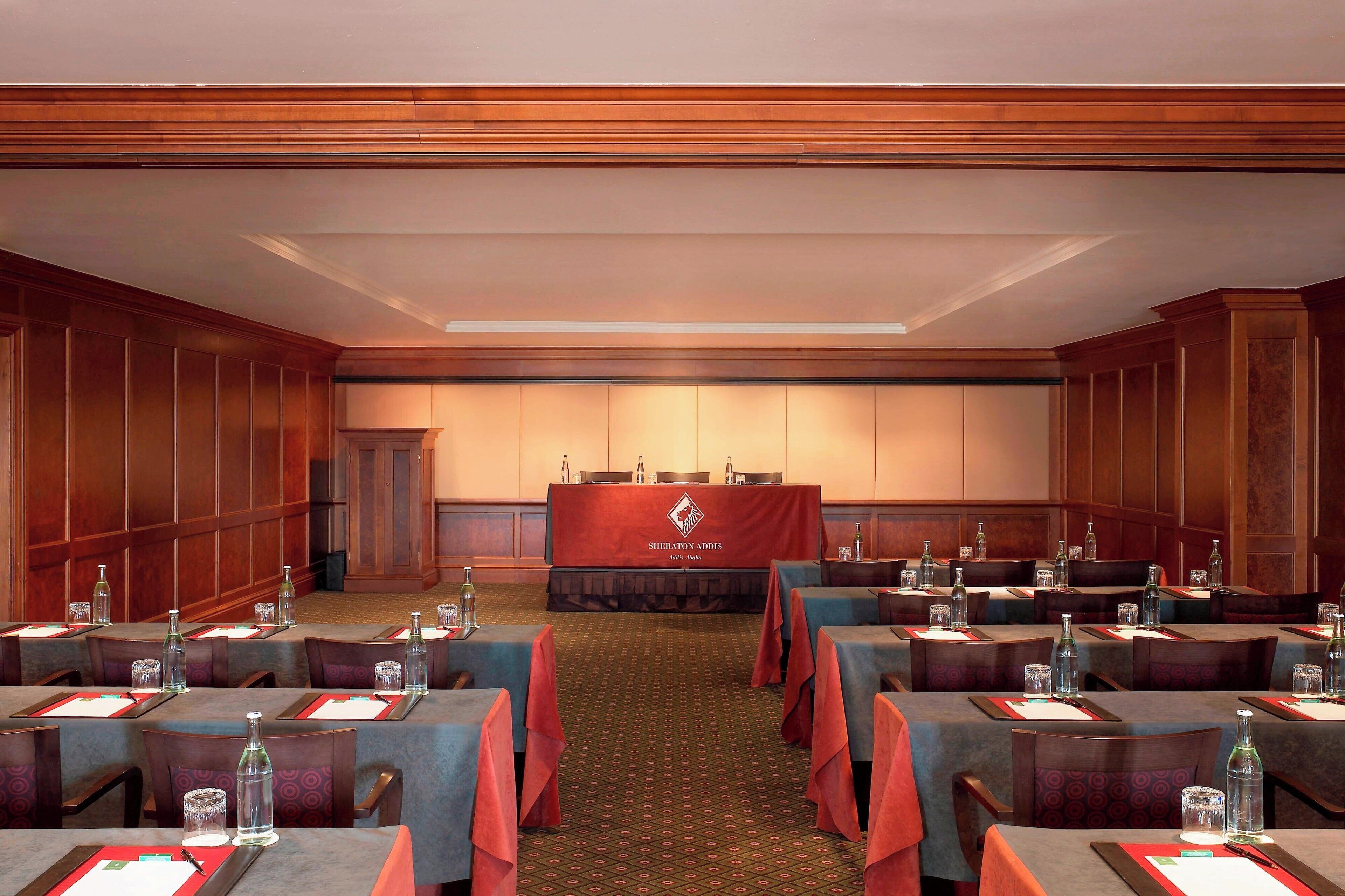 A conference room with tables set for meetings, a podium in the center, and a carpeted floor.