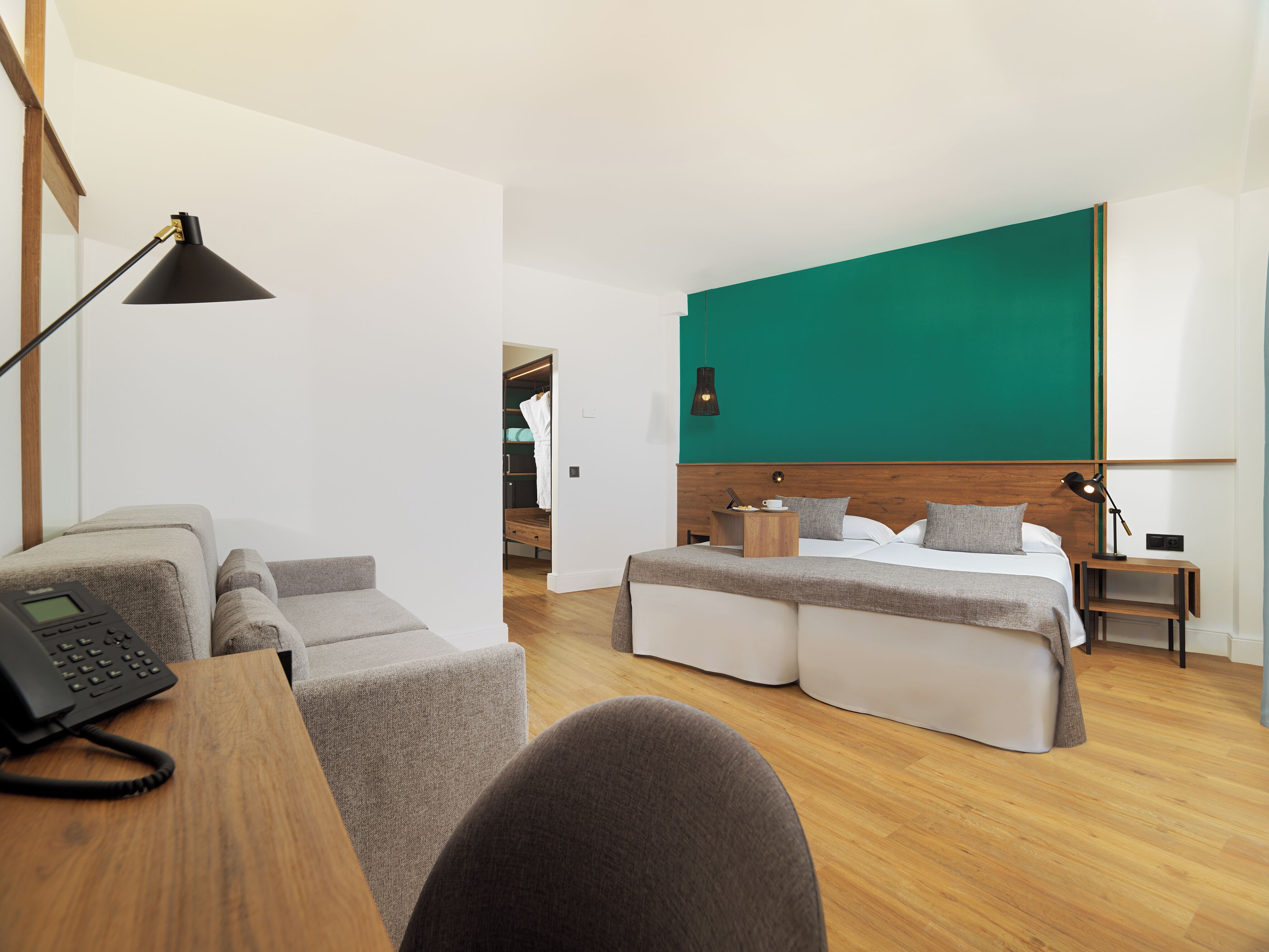 A modern hotel room with a bed, bedside tables, a desk with a phone, a chair, and a green accent wall.