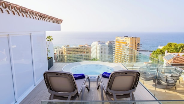 A balcony with a hot tub, two chairs, and a glass table.