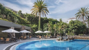 A swimming pool with lounge chairs and umbrellas, surrounded by lush greenery and palm trees.