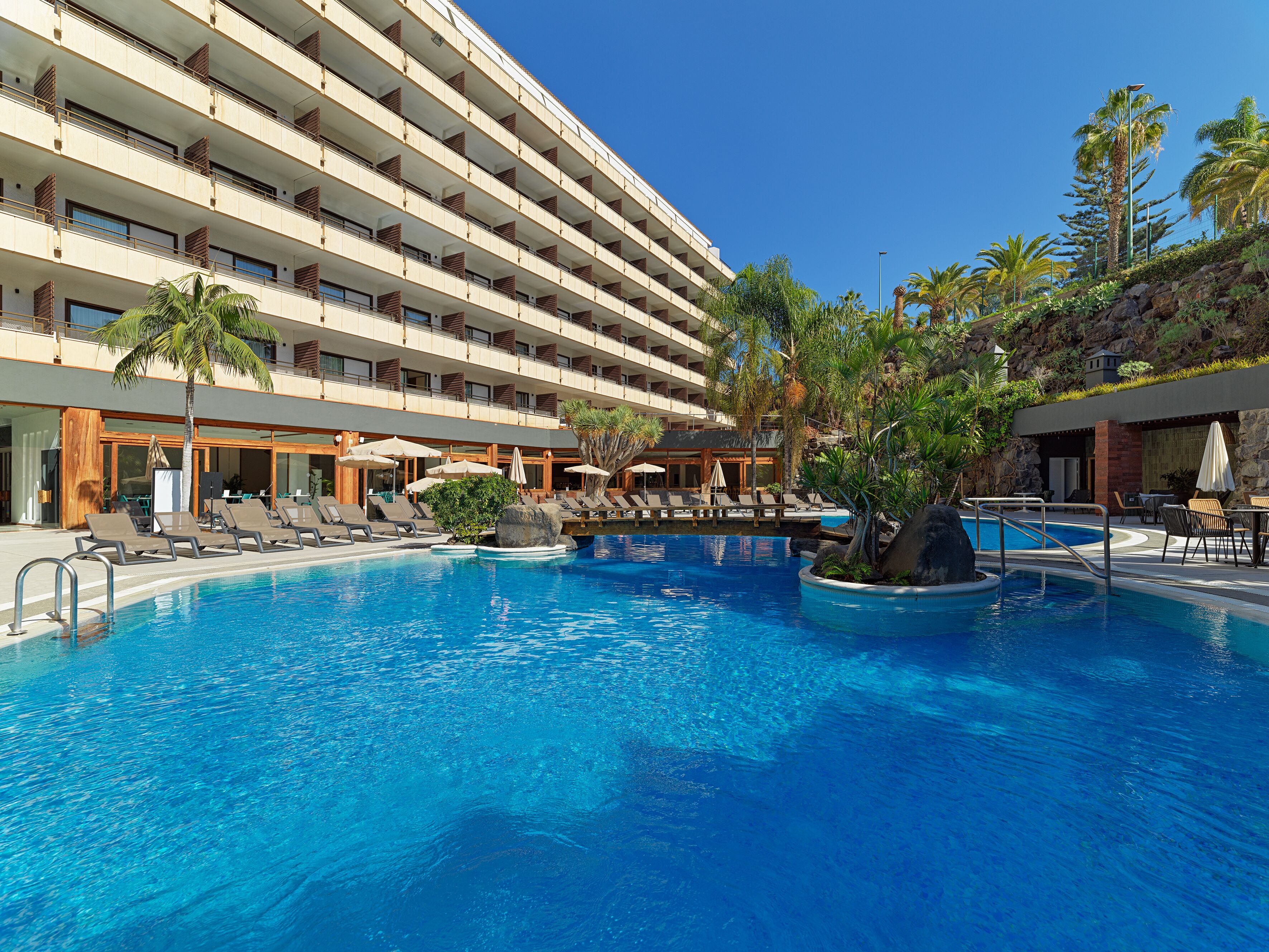 Un hôtel doté d’une grande piscine, de nombreux balcons et d’un espace extérieur aménagé pour s’asseoir.