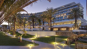 Un hotel de varios pisos con áreas de estar al aire libre, palmeras y un camino bien iluminado.