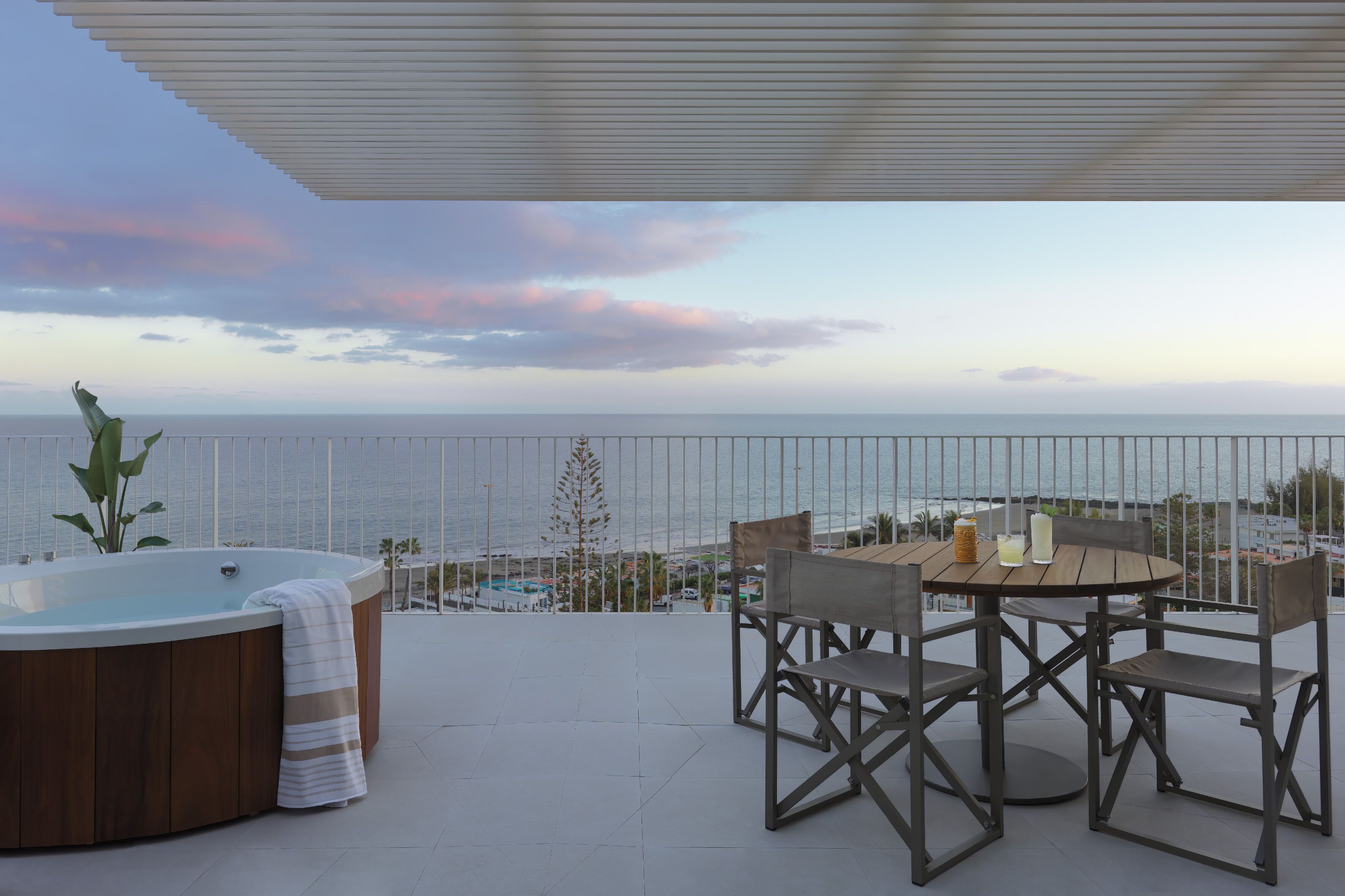 Una terraza con un jacuzzi, una mesa con sillas y vistas al mar.