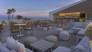 Un bar en la azotea con vistas al océano, que cuenta con mesas al aire libre y una zona de bar.
