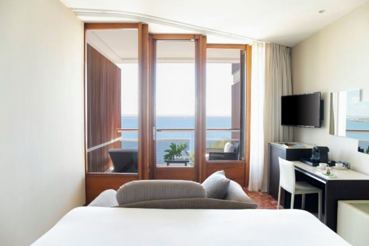 Habitación de hotel con cama, escritorio, televisión y balcón con vista al mar.