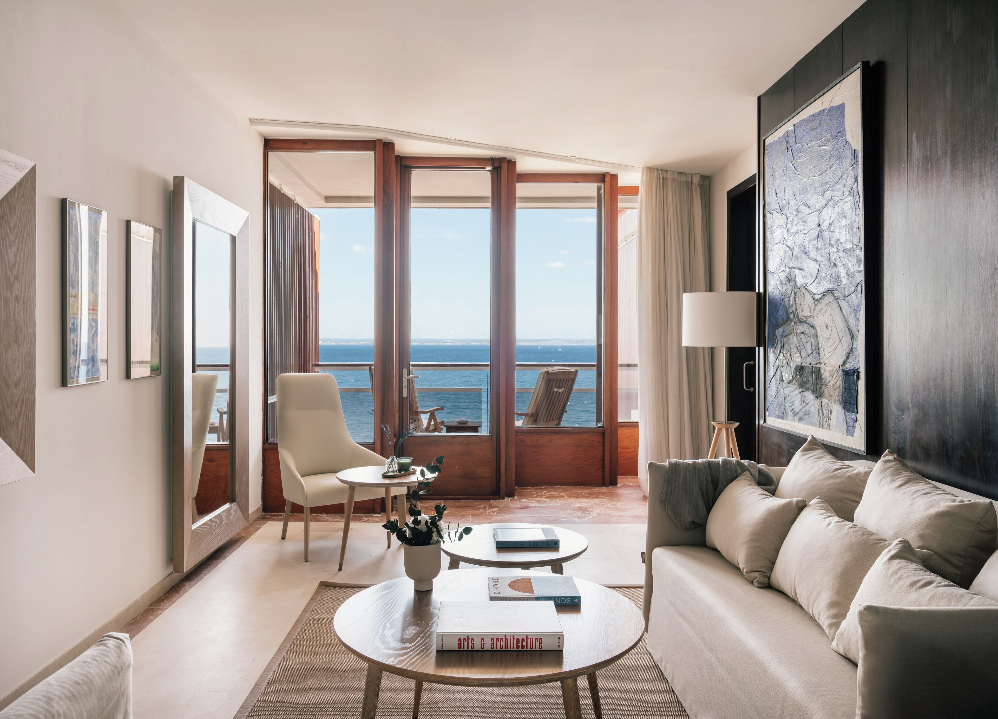 Habitación de hotel moderna con balcón, sofá, sillón y mesa de centro.