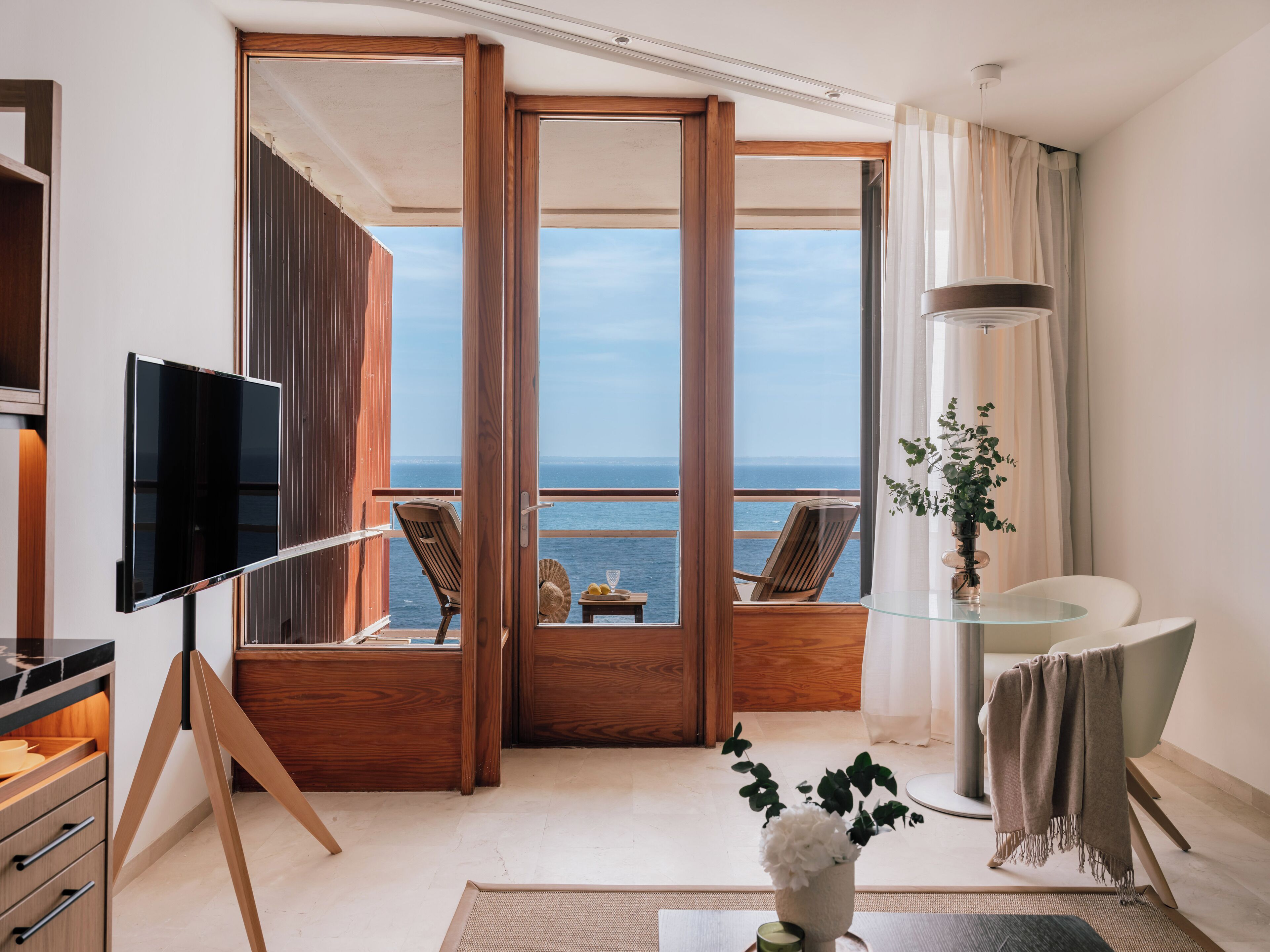 A modern room with a large window, a flat-screen TV, a glass table, and a potted plant.