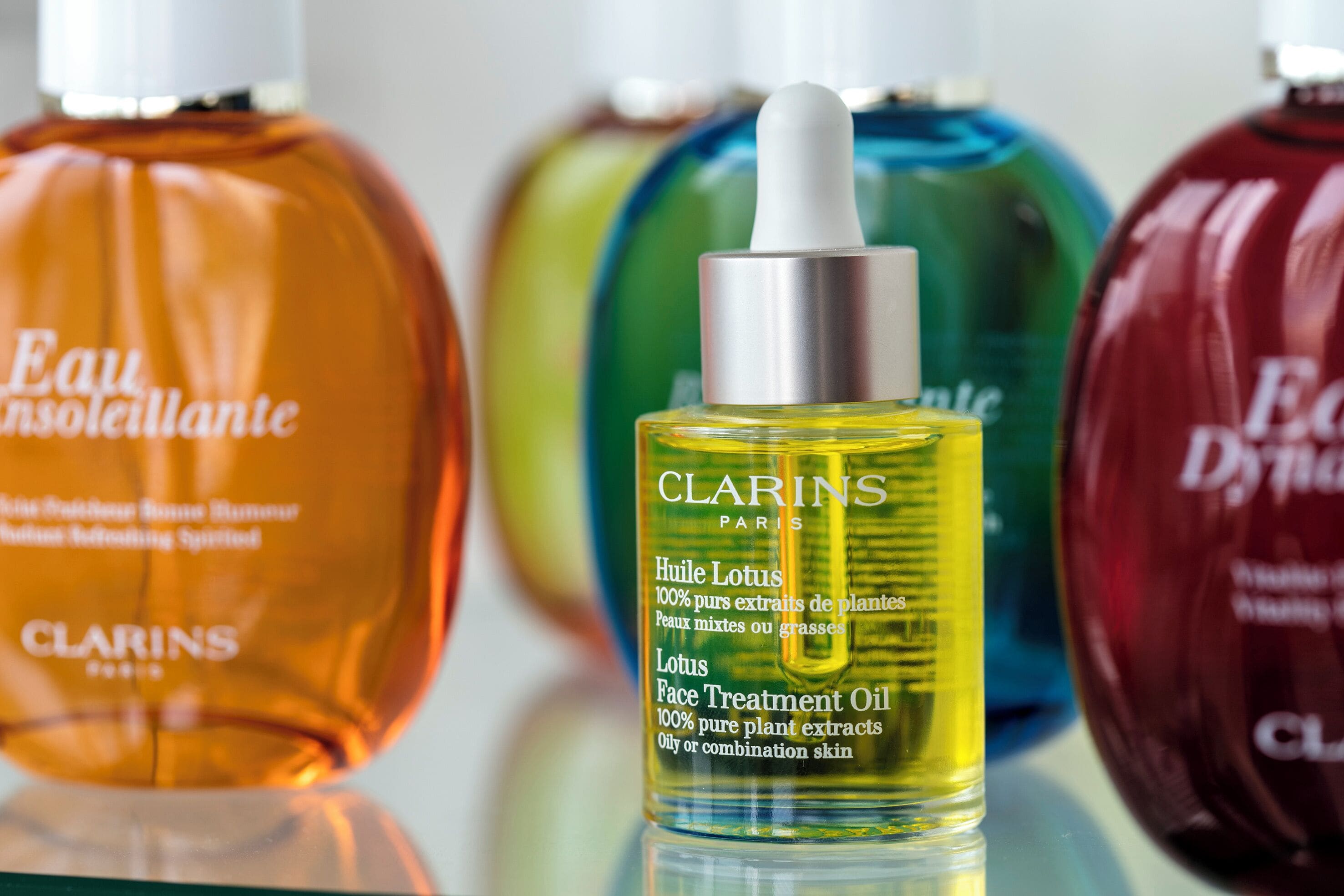 A variety of skincare products, including Clarins Paris lotion and other items, displayed on a reflective surface.