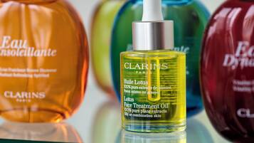 A variety of skincare products, including Clarins Paris lotion and other items, displayed on a reflective surface.