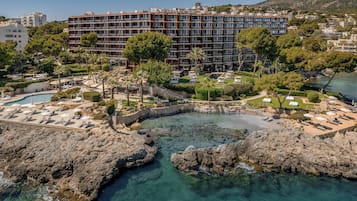 A coastal resort with a large building, a swimming pool, and a rocky shoreline.