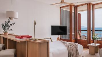 Un dormitorio moderno con una cama, un escritorio con libros, un televisor y un balcón con vista al mar.