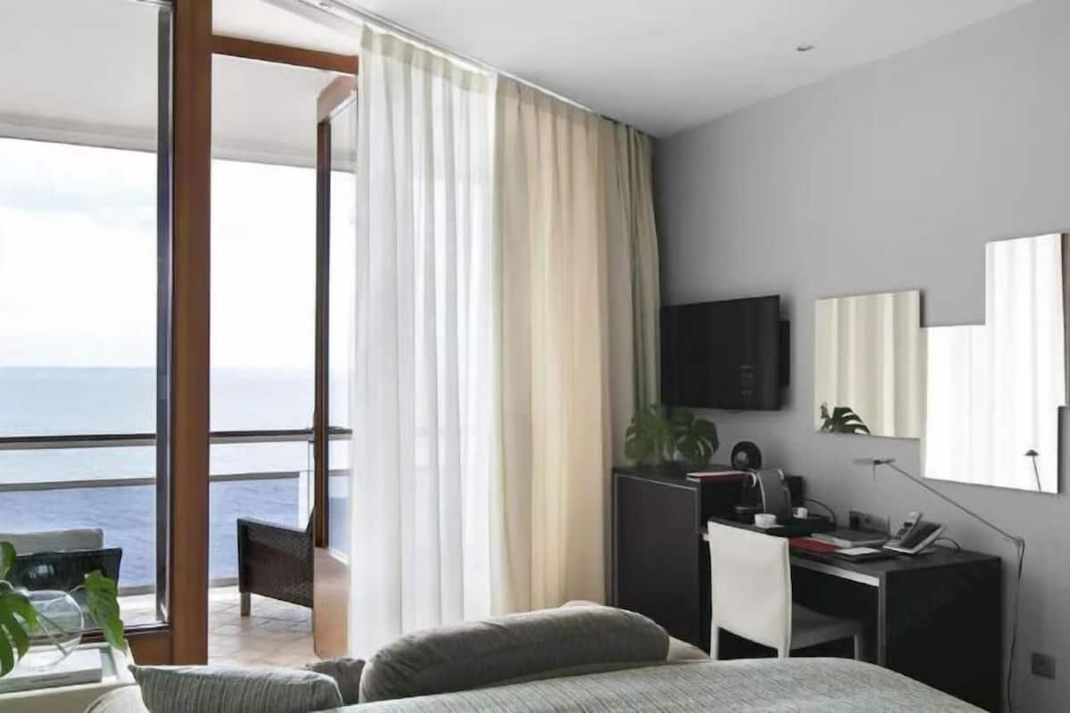 A modern hotel room with a balcony, a bed, a desk, and a TV.